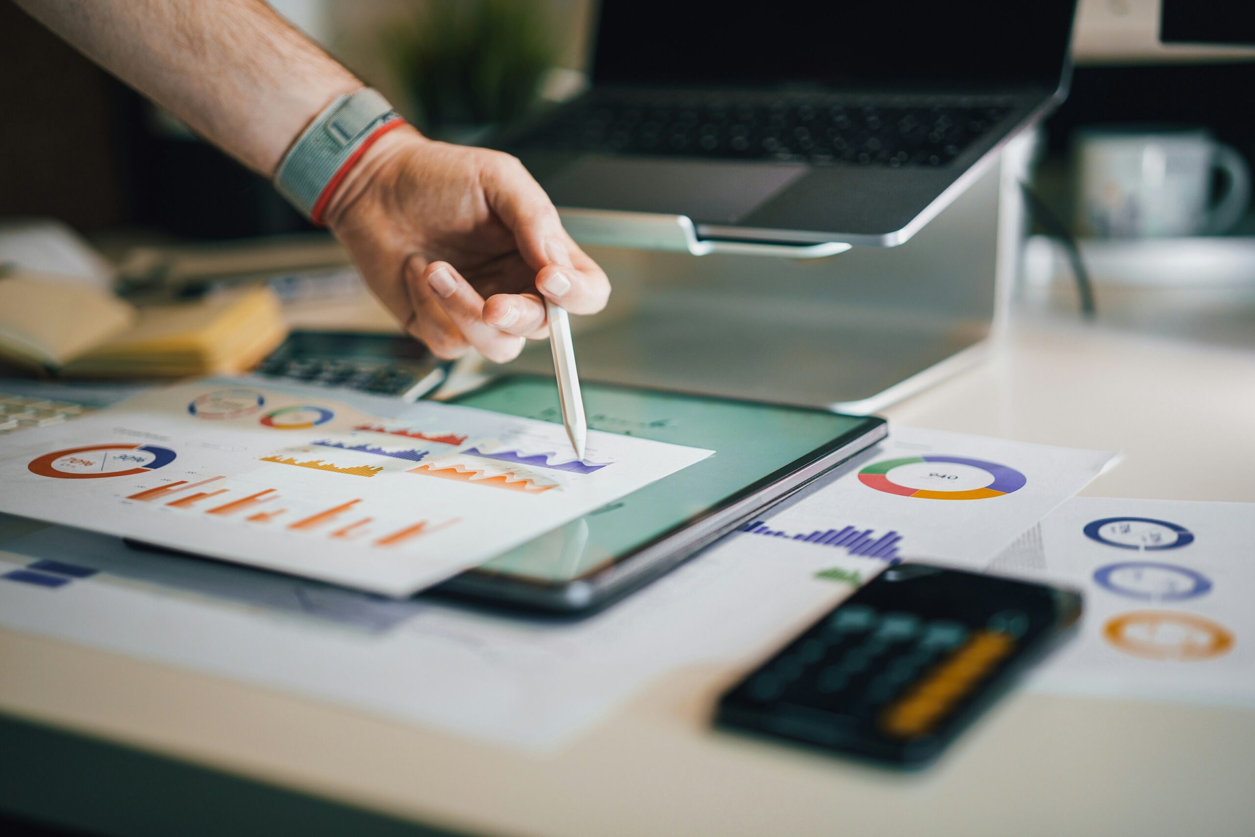 Main pointant avec un stylet vers des graphiques statistiques imprimés sur un bureau