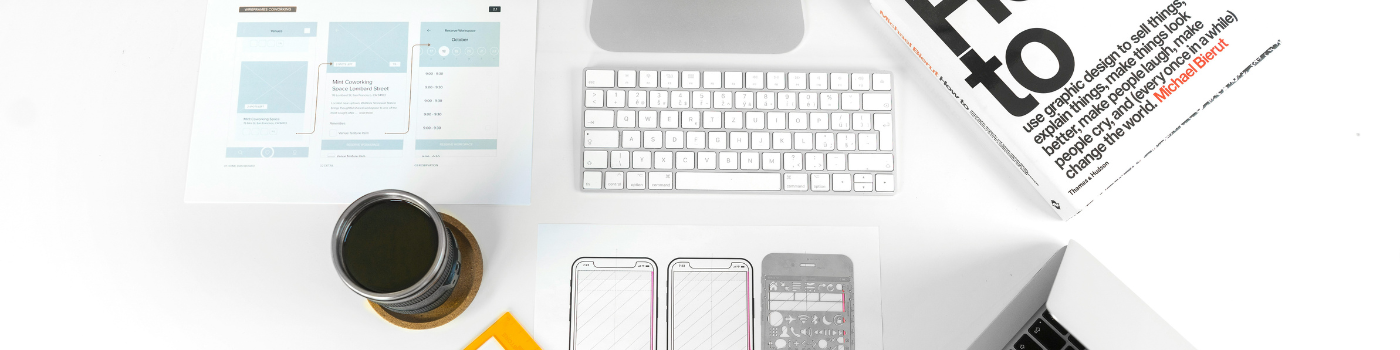 Bureau de designer UX/UI avec iMac, ordinateur portable, wireframes papier et gabarit de conception mobile orange.