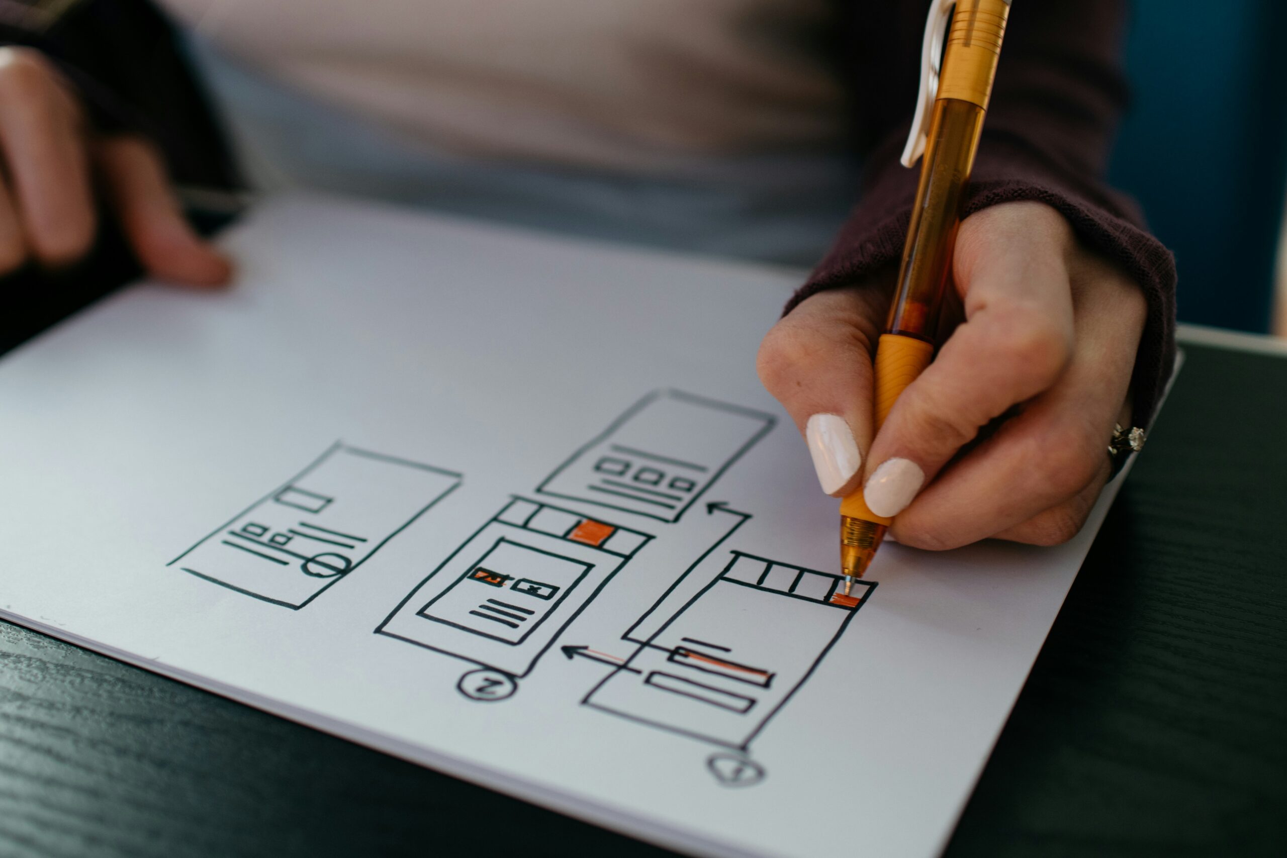 Gros plan sur une personne dessinant les maquettes filaires d'une interface utilisateur au stylo sur une feuille de papier